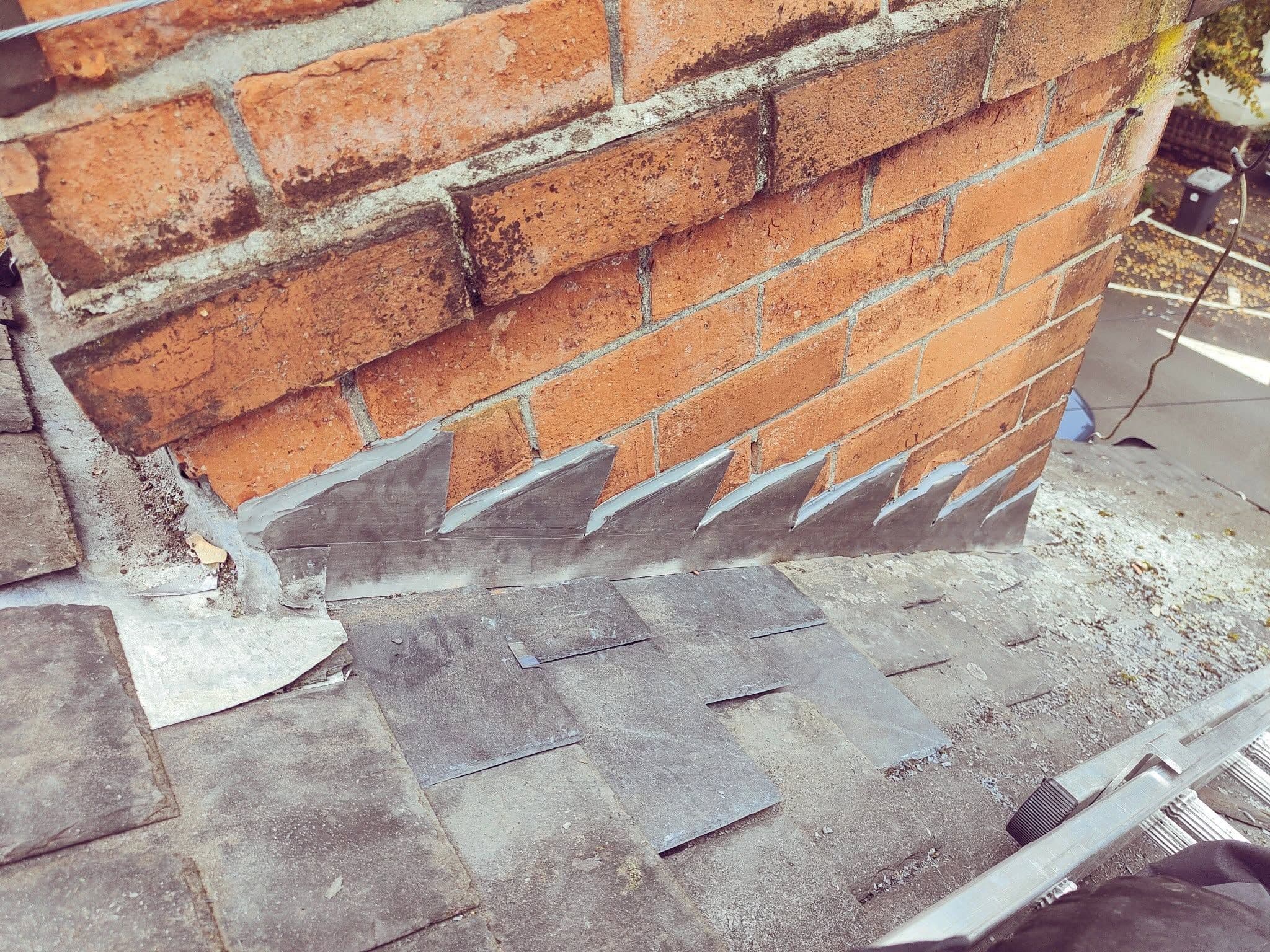 Lead soaker repair at the base of a brick chimney stack, with new lead flashing fitted between slate tiles